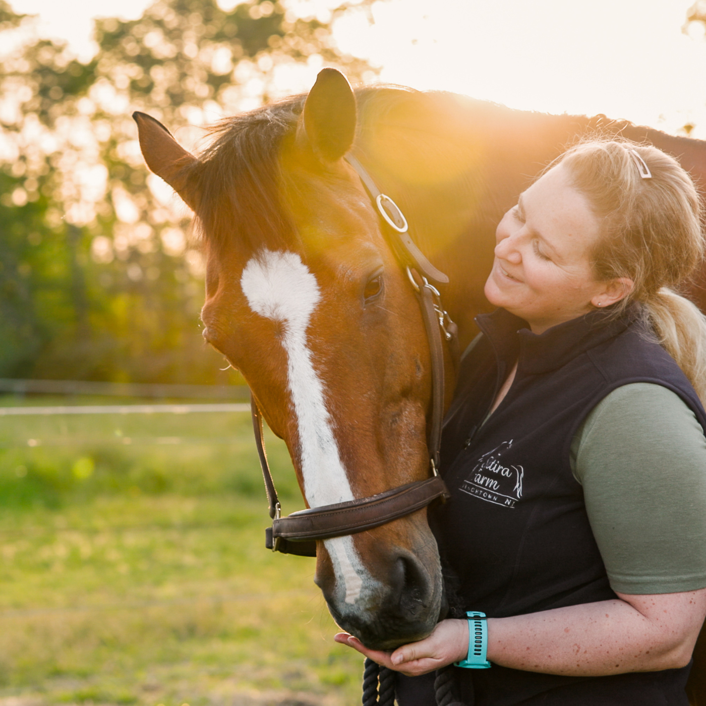 A StableFeed client, Adrienne Meisner smiling and petting her horse's muzzle.