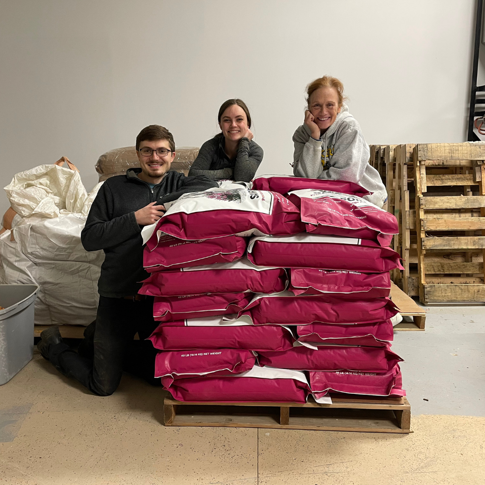 The StableFeed team smiling standing around a pallet of sainfoin forage pellet.